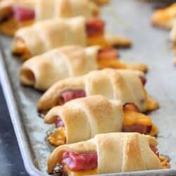 Golden brown crescent rolls filled with ham and melted cheese are lined up on a baking sheet.