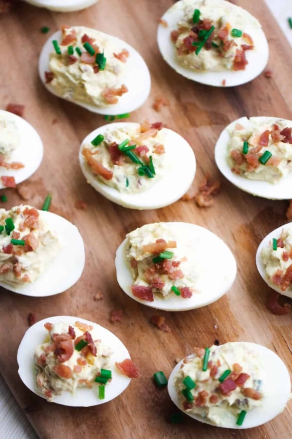 Deviled eggs topped with bacon and chives on a wooden board.