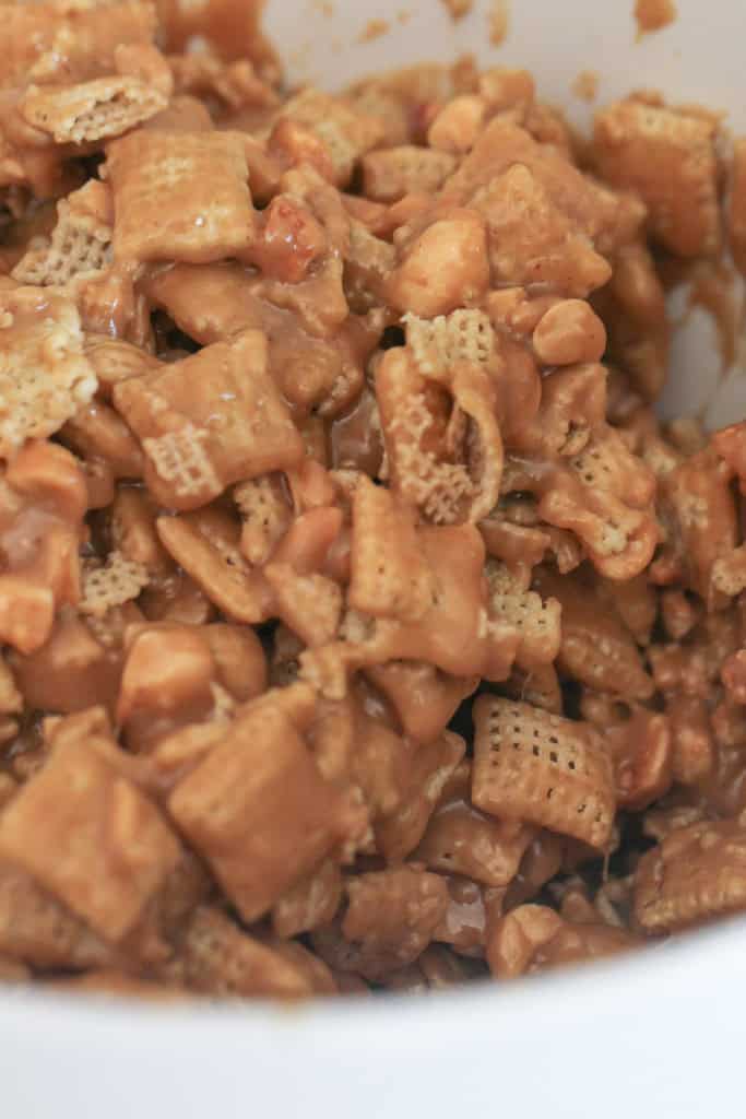 Chex mix covered in the peanut butter mixture in a mixing bowl.