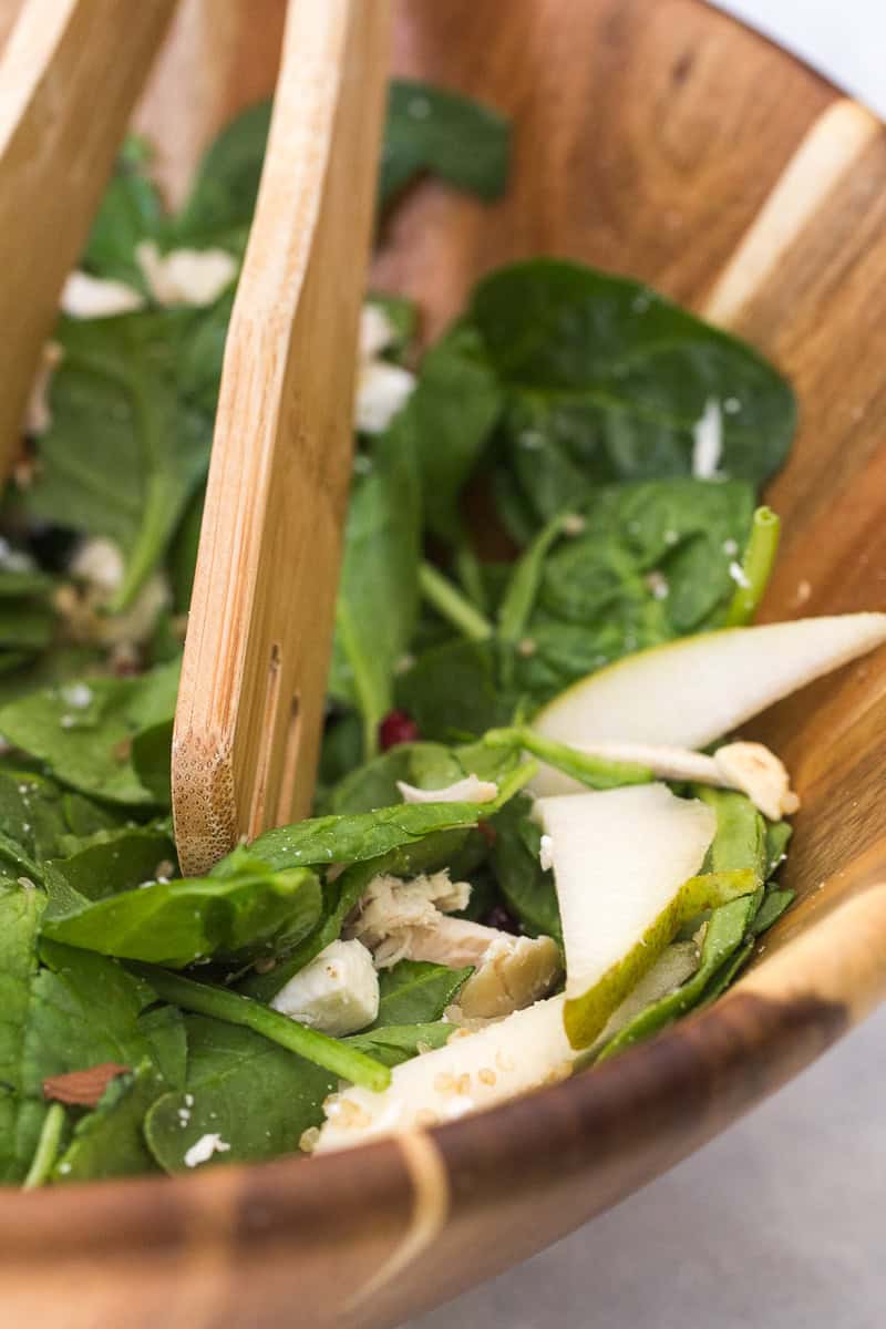 green salad in a wooden bowl being mixed together