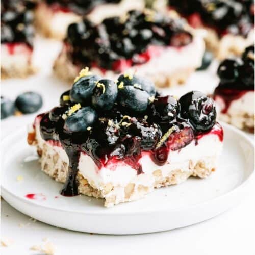 A square of Blueberry Jamboree on a white plate topped with fresh blueberries and lemon zest.