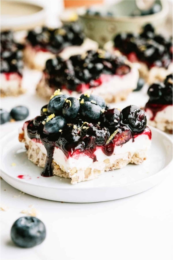 A square of Blueberry Jamboree on a white plate topped with fresh blueberries and lemon zest.