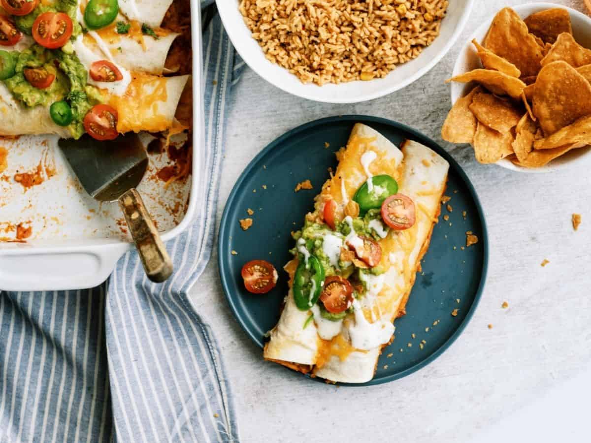 Slow Cooker Ranch Chicken Enchiladas on a blue plate next to the pan of Enchiladas