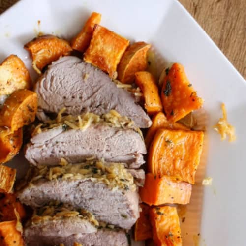 Sliced roast pork with a shredded herb topping, served with roasted sweet potato chunks on a white plate.