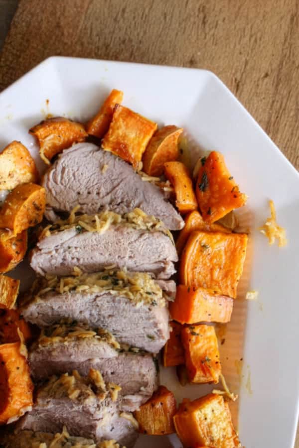Sliced roast pork with a shredded herb topping, served with roasted sweet potato chunks on a white plate.