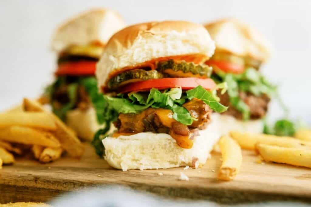 Front view of baked cheeseburger sliders on a cutting board with french fries.