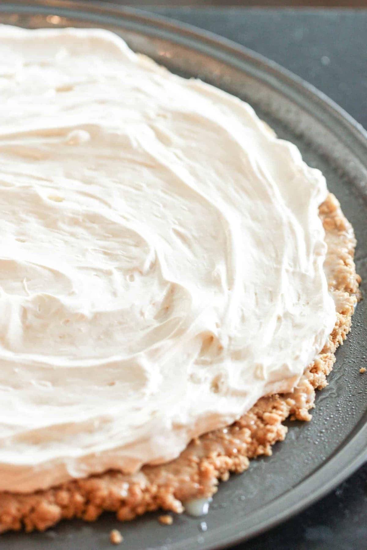 A pizza pan with a crust topped with a thick layer of creamy white frosting or whipped topping.