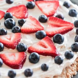 A dessert pizza topped with a cream cheese layer, fresh sliced strawberries, and whole blueberries on a round crust.