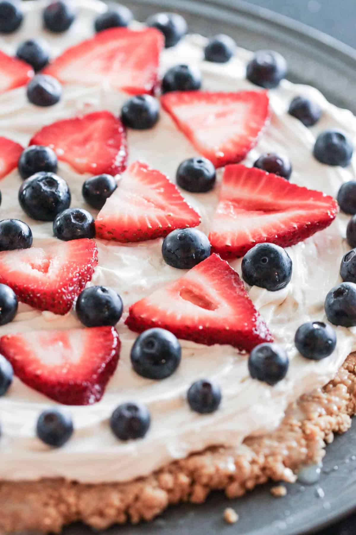 A dessert pizza topped with a cream cheese layer, fresh sliced strawberries, and whole blueberries on a round crust.