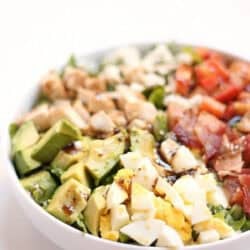 A bowl of Cobb salad with chopped avocado, hard-boiled egg, chicken, bacon, and tomato arranged in sections.