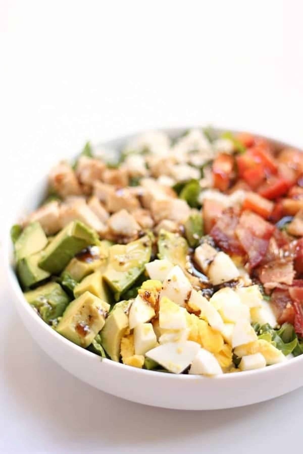 A bowl of Cobb salad with chopped avocado, hard-boiled egg, chicken, bacon, and tomato arranged in sections.
