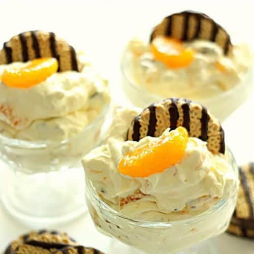Three glass dessert cups filled with creamy mousse, each topped with a chocolate-striped cookie and a mandarin orange slice.