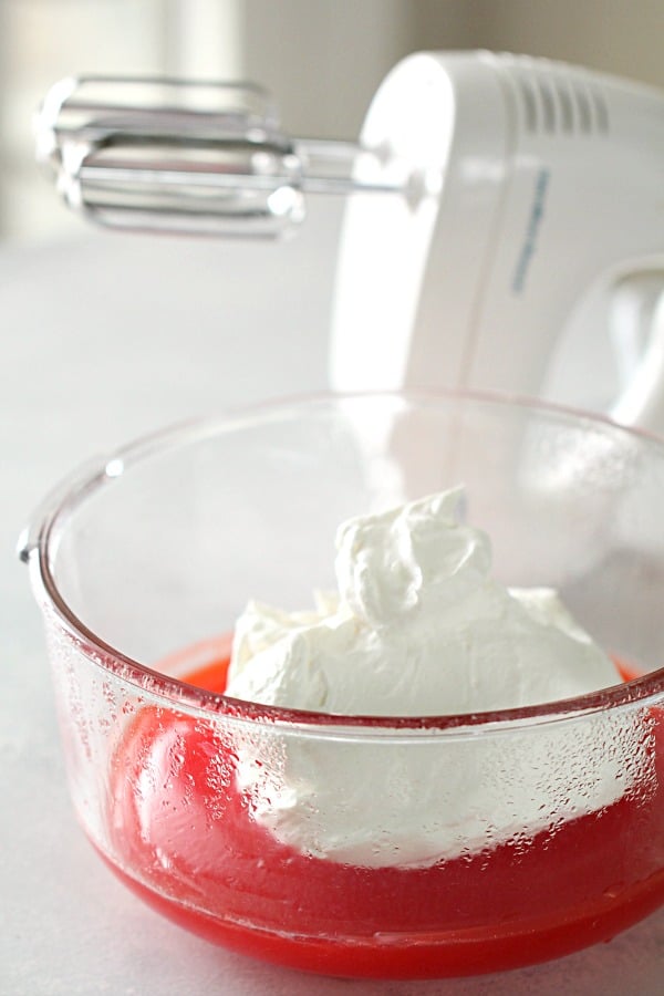 Jello in a bowl with whipped cream on top and an electric mixer in the back