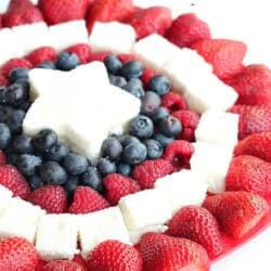 A plate arranged with strawberries, raspberries, blueberries, and square pieces of white cake, with a star-shaped cake piece in the center, forming a patriotic pattern.