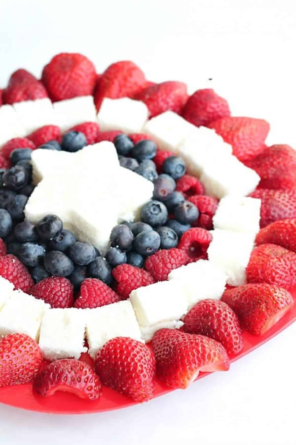 A plate arranged with strawberries, raspberries, blueberries, and square pieces of white cake, with a star-shaped cake piece in the center, forming a patriotic pattern.