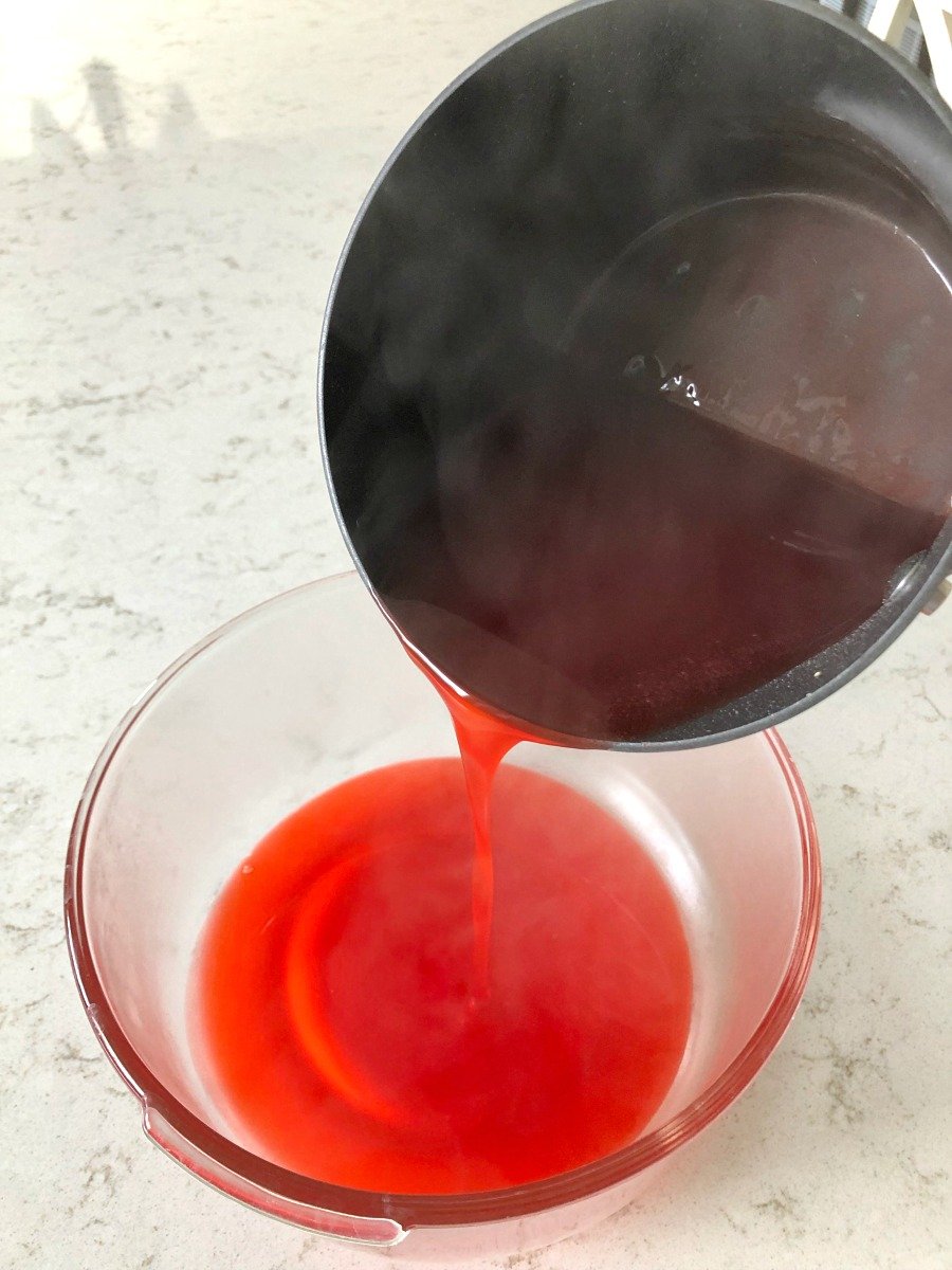 liquid jello being poured from a saucepan into a glass bowl