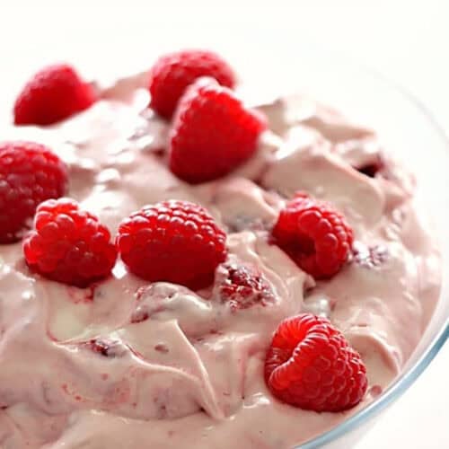 A glass bowl filled with creamy pink raspberry mousse, topped with several fresh raspberries.