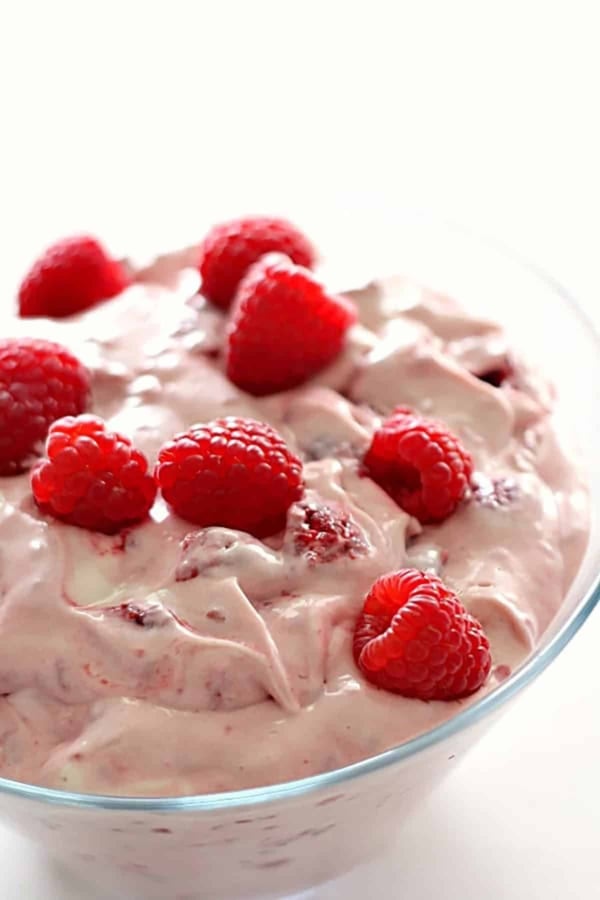 A glass bowl filled with creamy pink raspberry mousse, topped with several fresh raspberries.