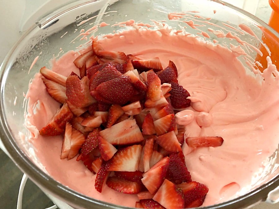 whipped pink jello in a glass bowl with fresh strawberries dumped on top