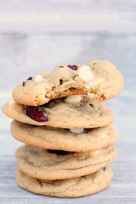 A stack of four cookies with white chocolate chips and dried cranberries, with a bite taken out of the top cookie.