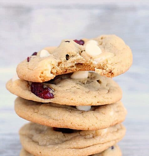 A stack of four cookies with white chocolate chips and dried cranberries, with a bite taken out of the top cookie.