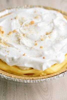 A close-up of a cream pie with a golden crust and a topping of whipped cream and sprinkled crumbs.