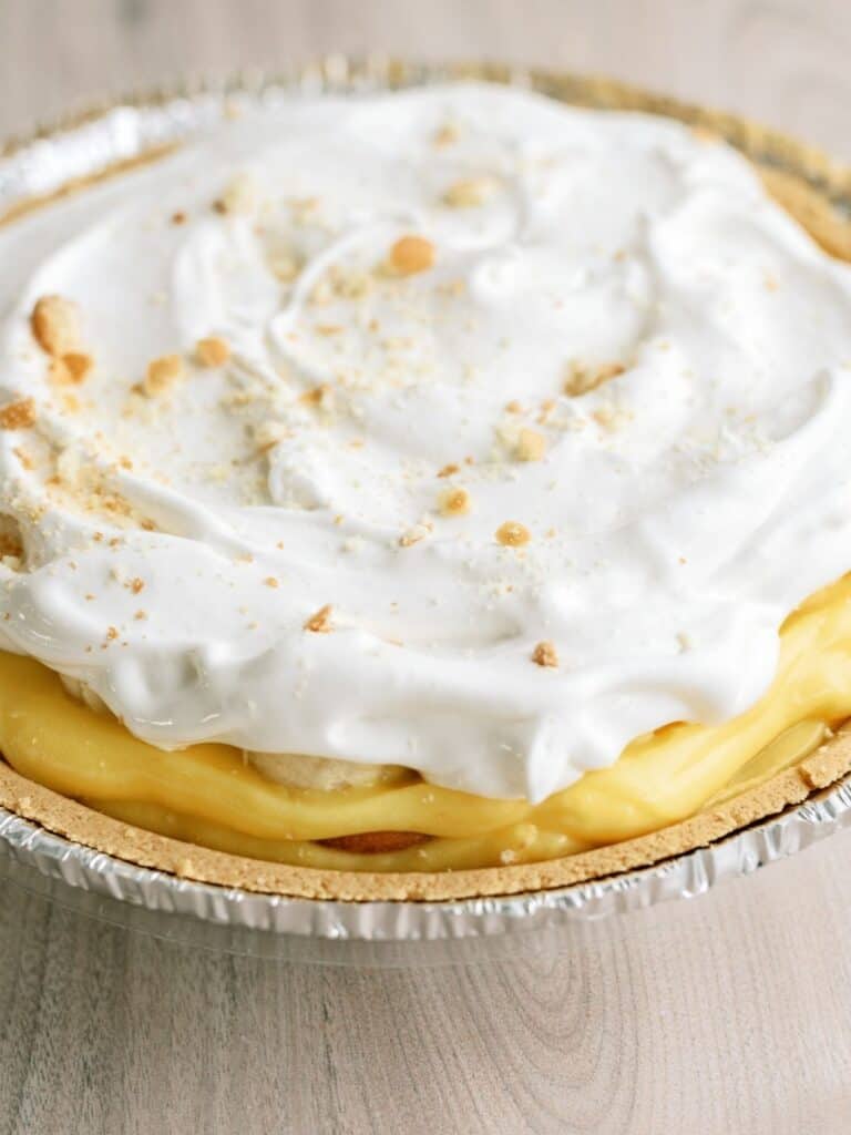 A close-up of a cream pie with a golden crust and a topping of whipped cream and sprinkled crumbs.