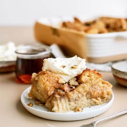 A slice of Brown Sugar and Maple Bread Pudding on a plate topped with whip cream.