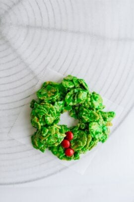A festive green cornflake wreath with red candy decorations arranged on a white surface.