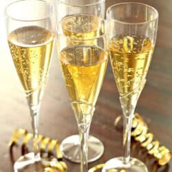 Four champagne flutes filled with sparkling wine are placed on a wooden surface, surrounded by gold ribbon decorations.
