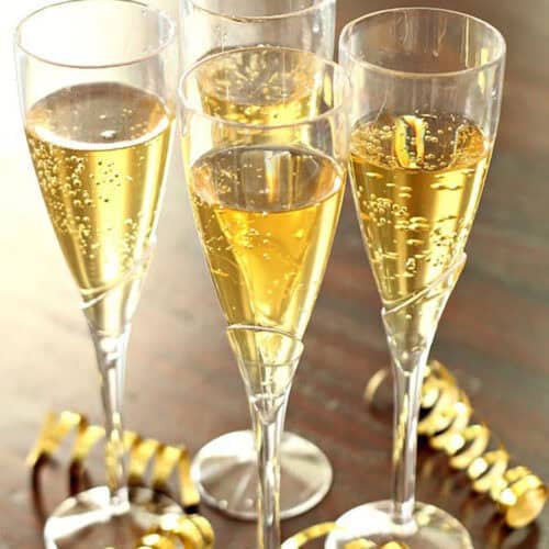 Four champagne flutes filled with sparkling wine are placed on a wooden surface, surrounded by gold ribbon decorations.