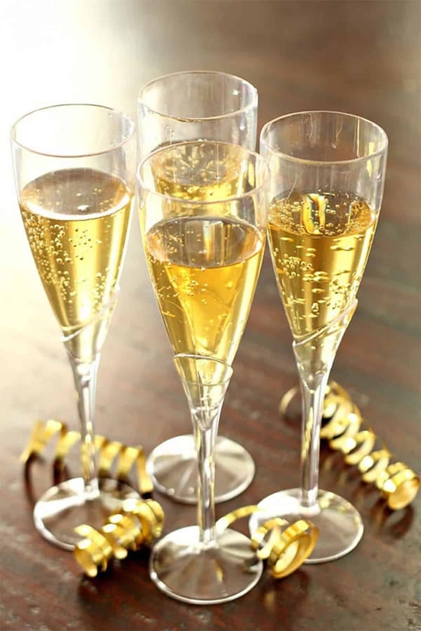Four champagne flutes filled with sparkling wine are placed on a wooden surface, surrounded by gold ribbon decorations.