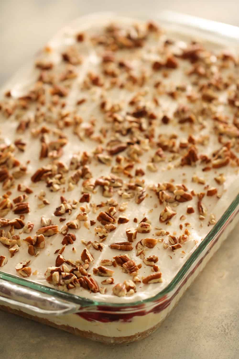 cool whip topped with pecans on top of layered cheesecake dessert