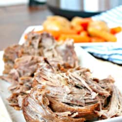 Tender, juicy pot roast served with vegetables on a white platter.