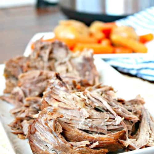 Tender, juicy pot roast served with vegetables on a white platter.