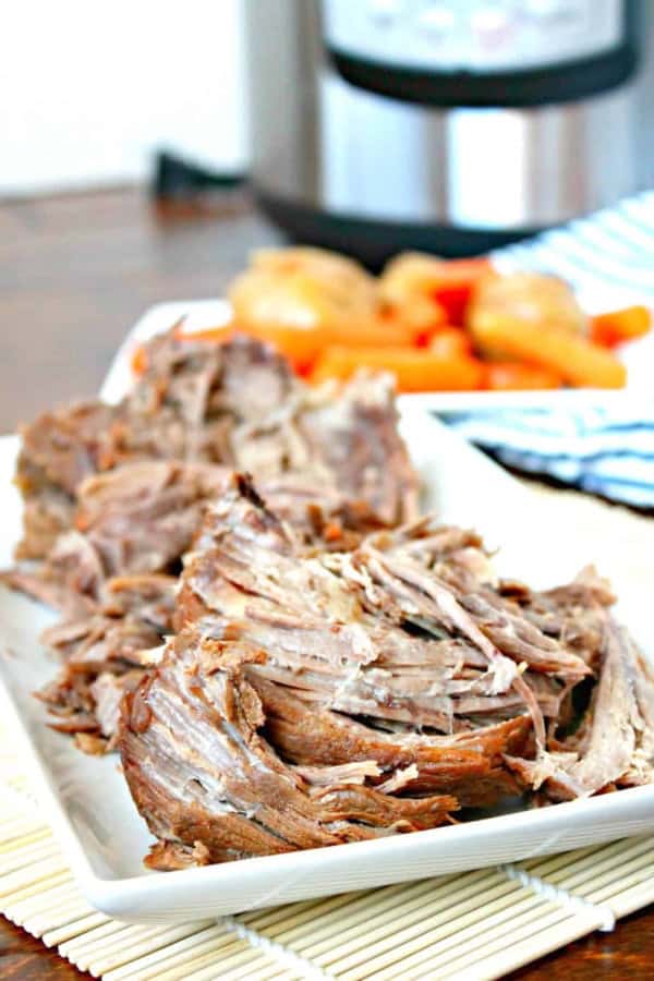 Tender, juicy pot roast served with vegetables on a white platter.