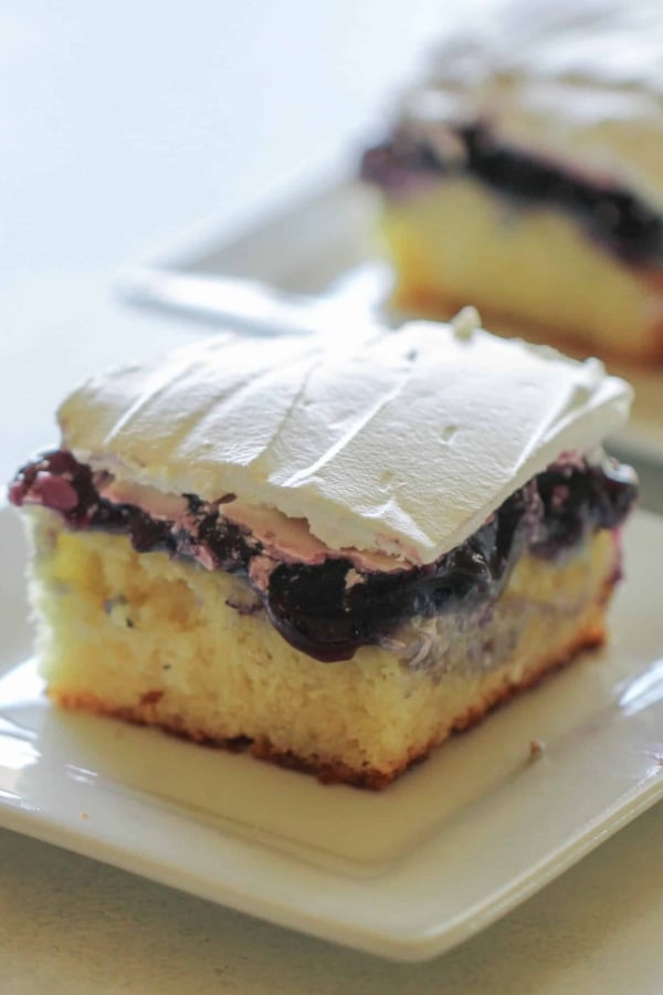 Slices of Blueberry Cheesecake Pudding Poke Cake on small white plates.