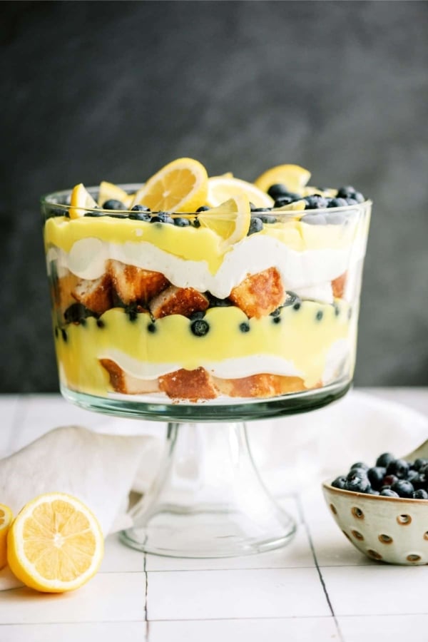 Lemon Blueberry Trifle in a trifle dish with a lemon and small bowl of blueberries on next to it.