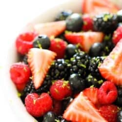 A close-up of a bowl filled with fresh strawberries, raspberries, blackberries, and blueberries, topped with grated lime zest.