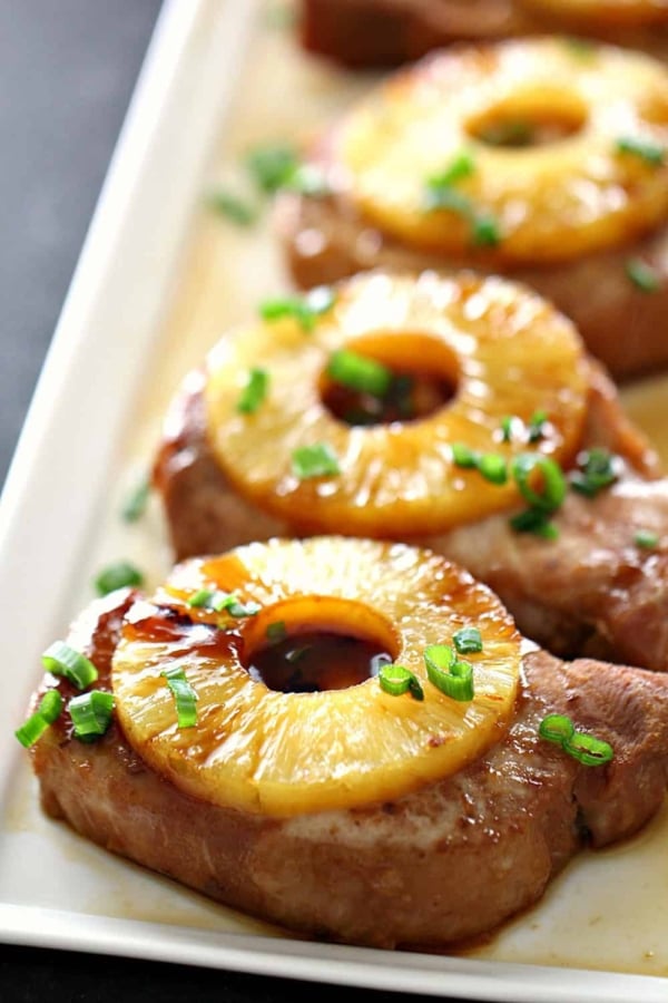 Close-up of a platter featuring pork chops topped with pineapple rings and garnished with sliced green onions.