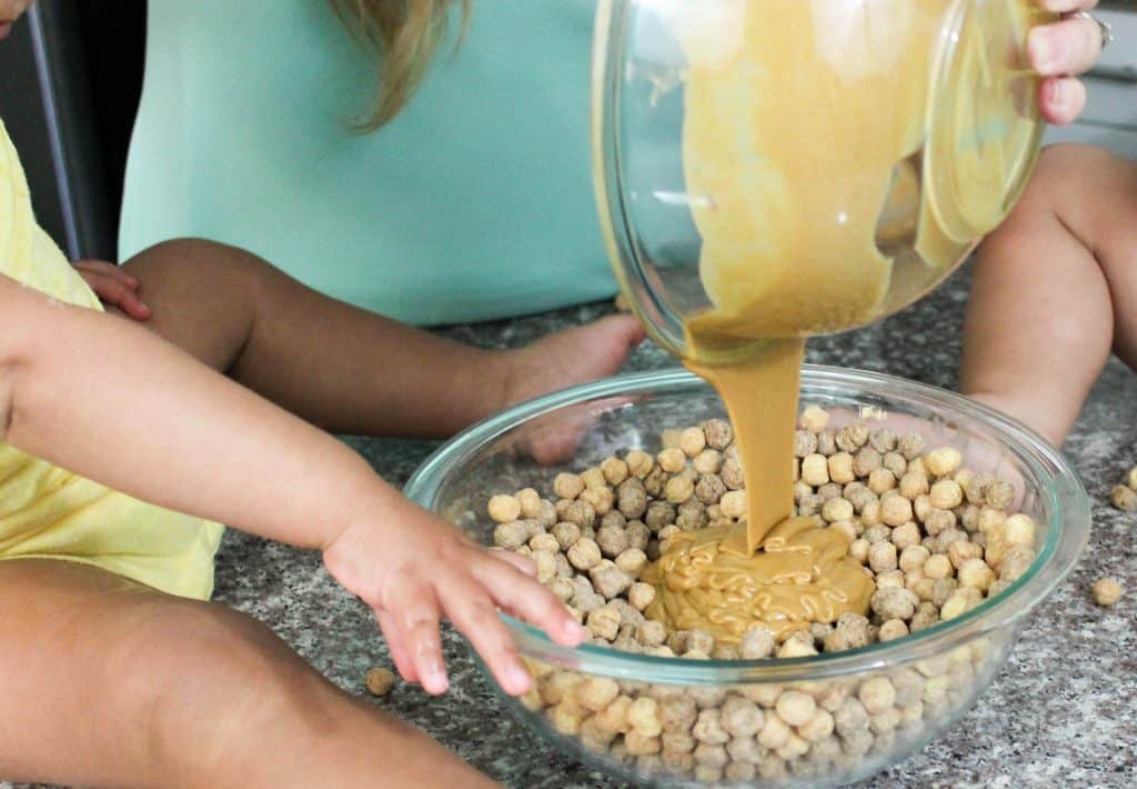 Pouring Peanut Butter Mixture into a bowl of Reese's Puffs