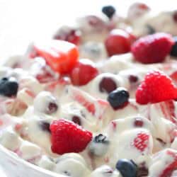 A close-up of a bowl filled with mixed berries, including strawberries, raspberries, and blueberries, coated in a creamy white sauce.