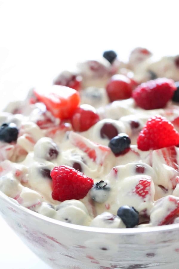 A close-up of a bowl filled with mixed berries, including strawberries, raspberries, and blueberries, coated in a creamy white sauce.