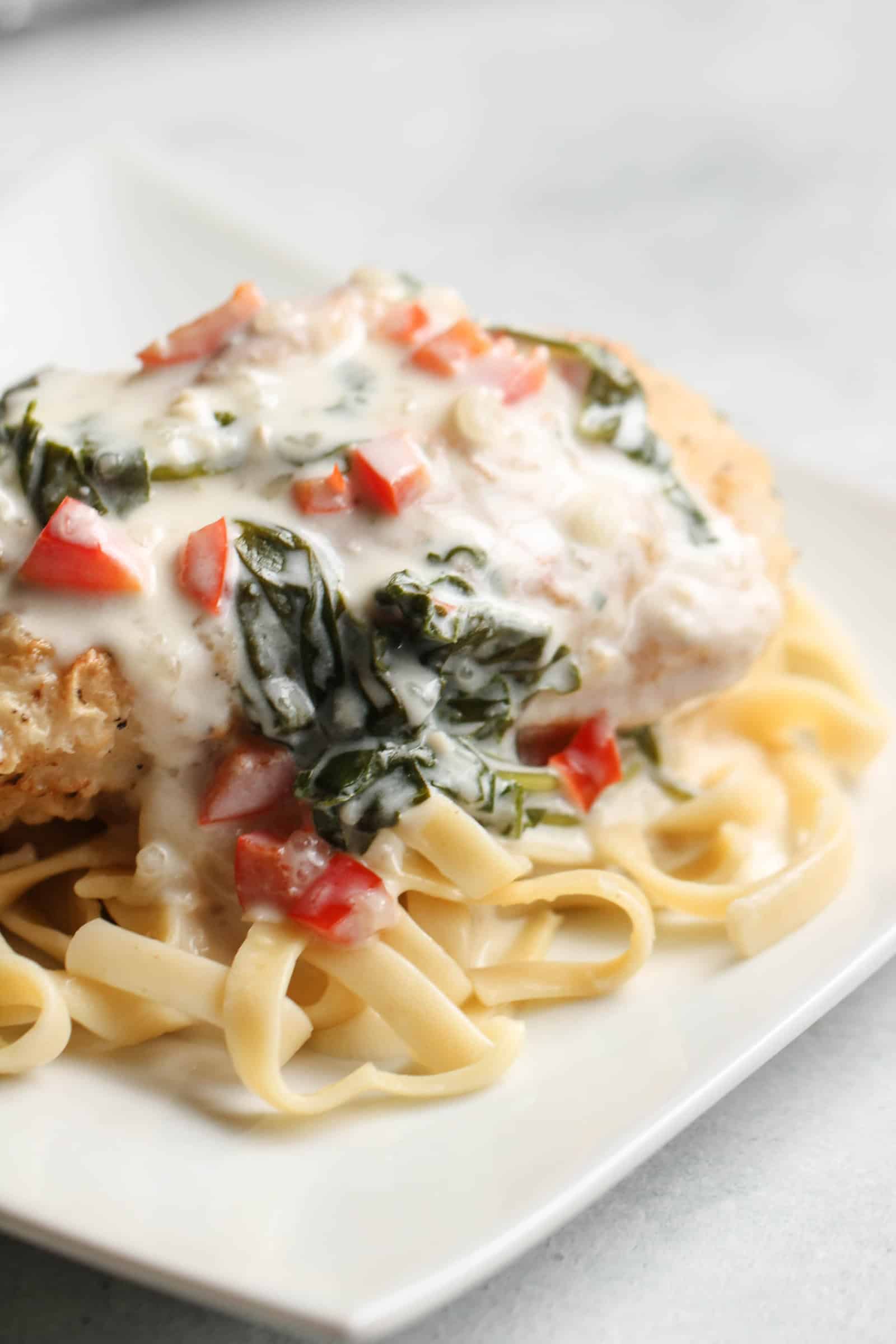 Tuscan Garlic Chicken served over fettuccine on a white plate