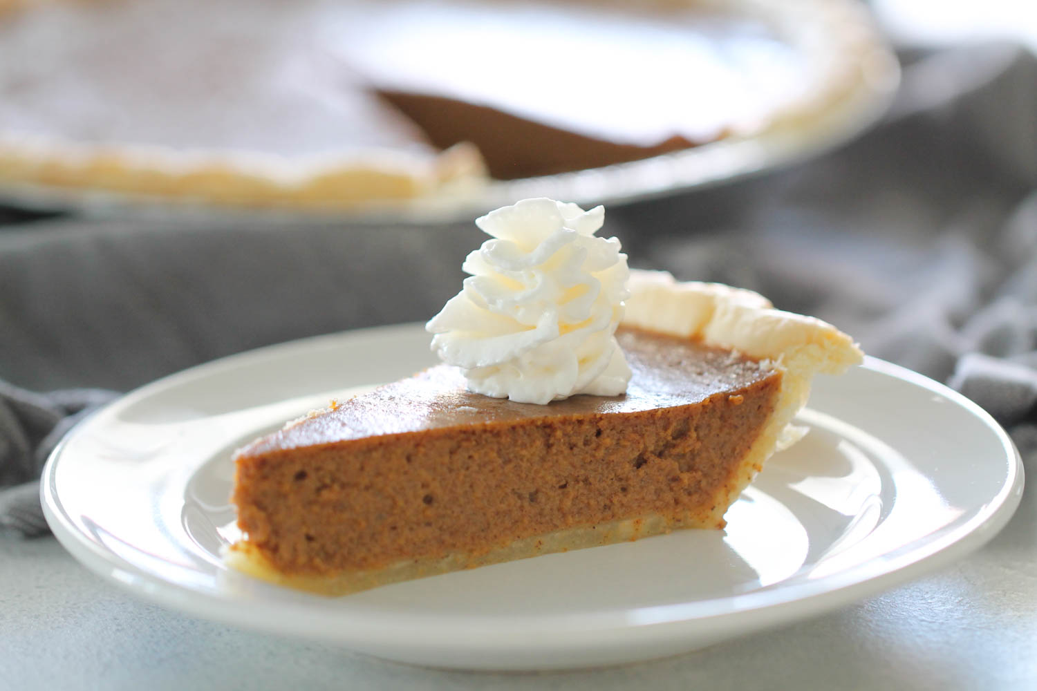Slice of pumpkin pie topped with whip cream on a white plate