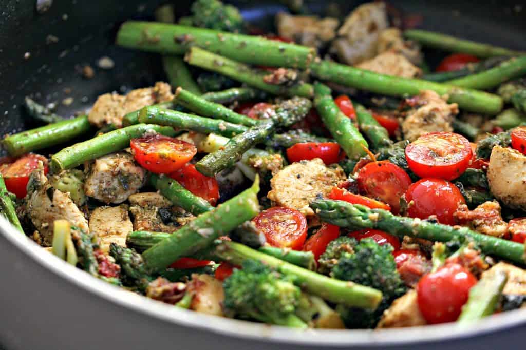 chicken, asparagus, tomatoes, and broccoli mixed together with pesto in a skillet