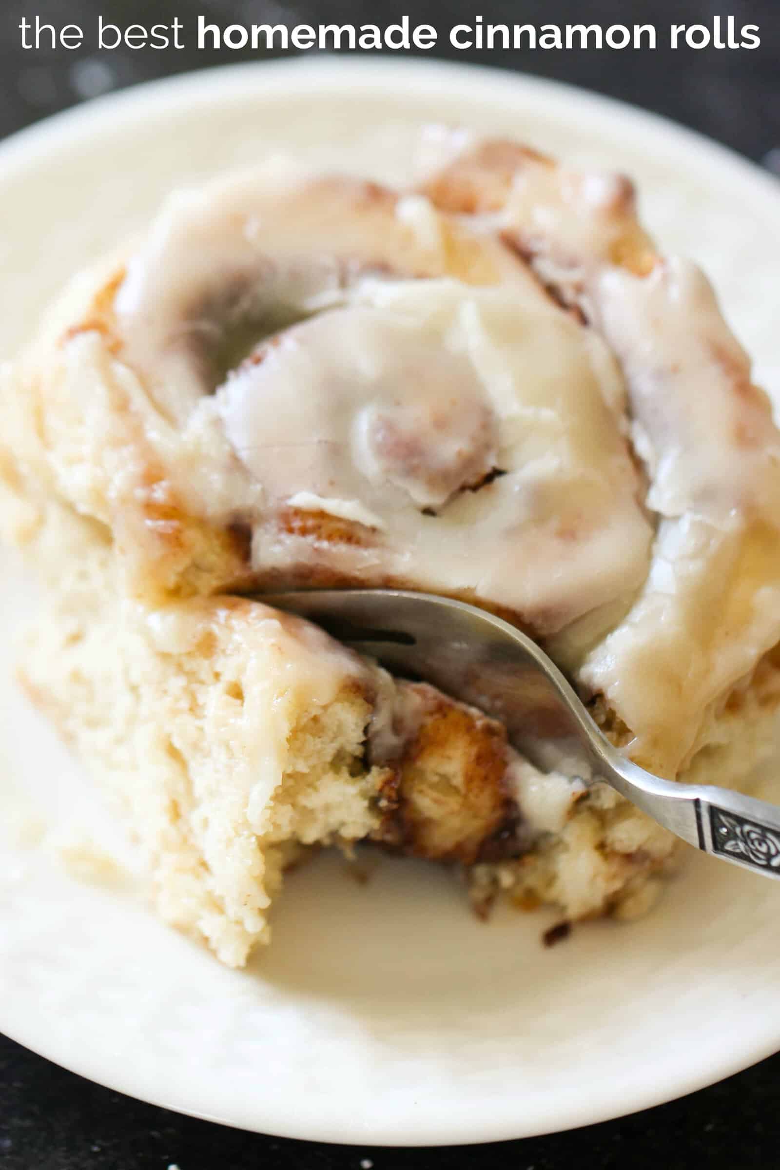 A fork slicing a bite out of a cinnamon roll on a plate