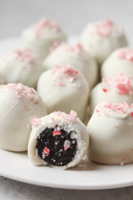 A plate of white chocolate-coated truffles, with one truffle cut in half to reveal a dark filling and pink sprinkles on top.