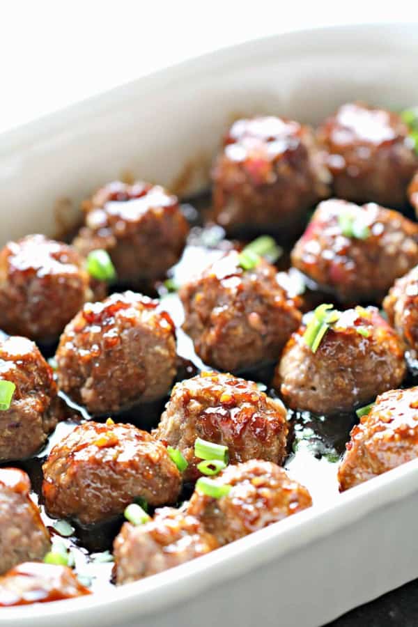 A baking dish filled with cooked glazed meatballs, garnished with chopped green onions.