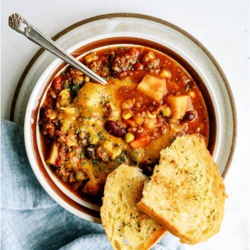A bowl of shepherd's pie chili topped with herbs, served with a spoon and two slices of toasted bread on the side.
